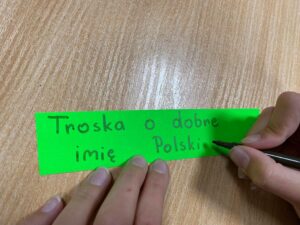 ręka dziecka pisząca "Troska o dobre imię Polski"